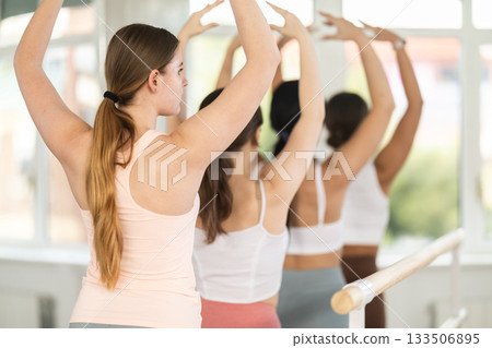 Young girl practicing fifth arm position holding by ballet barre 133506895