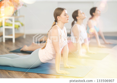 Young girl teaches yoga lesson, shows students technique of performing Urdhva Mukha Shvanasana asana Young girl teaches yoga lesson, shows students technique of performing Urdhva Mukha Shvanasana asana 133506907