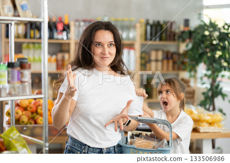 Tired and angry mother with basket of groceries in her hands quarreling with her little daughter. 133506986