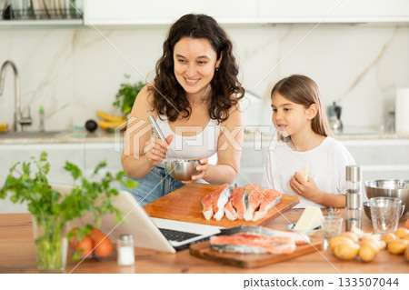 Happy mother and her daughter preparing salmon in the kitchen 133507044
