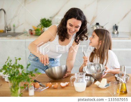 Happy mother and her daughter whisking ingredients in metal bowl in the kitchen Happy mother and her daughter whisking ingredients in metal bowl in the kitchen 133507055
