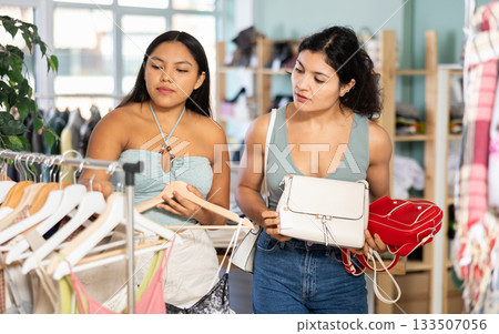 Two young woman chooses dresses or o tops and handbag for the summer period in fashionable clothing store 133507056