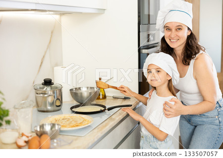 Mom and her daughter in white chief hats fry pancakes 133507057