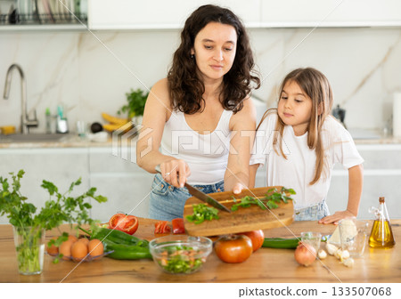 Mom and daughter dice up raw vegetables for salad on cutting boards. 133507068