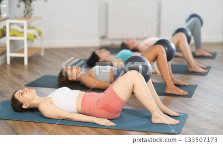 Young girl doing bridge exercise with ball group pilates session Young girl doing bridge exercise with ball group pilates session 133507173