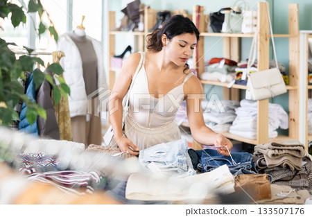 Positive young woman chooses fashionable shorts in clothing store Positive young woman chooses fashionable shorts in clothing store 133507176
