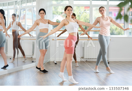 Confident young girl training ballet moves with group of youth people at ballet school Confident young girl training ballet moves with group of youth people at ballet school 133507346
