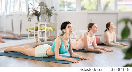 Young girl maintaining Sphinx Pose on mat during group yoga workout Young girl maintaining Sphinx Pose on mat during group yoga workout 133507356