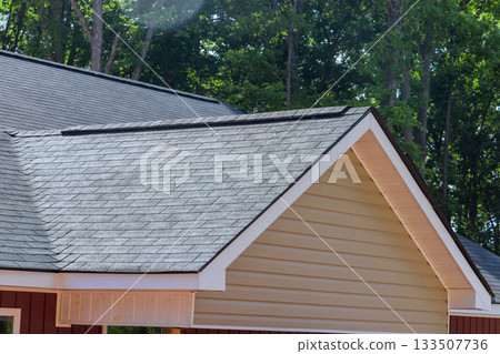Newly installed black shingle roof covers house nestled among trees on modern design. 133507736