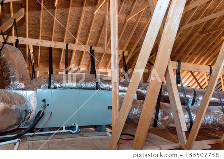 Workers are installing ductwork insulation in attic area of home during renovation. 133507738