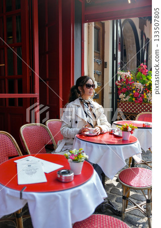 Woman in beige trench coat sitting at Paris street cafe Woman in beige trench coat sitting at Paris street cafe 133507805