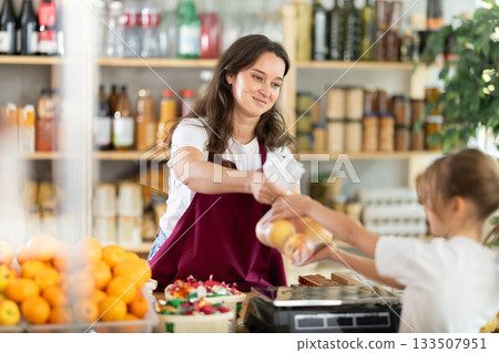 Girl buys ripe apples. Positive female seller weighs apples on scales 133507951