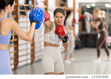 Young girl training boxing kicks on punch mitts 133507956
