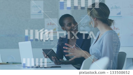 Reviewing two colleagues in business attire analyzing charts on tablet and laptop at office table Reviewing two colleagues in business attire analyzing charts on tablet and laptop at office table 133508652