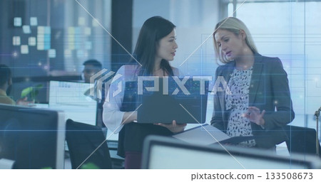 Reviewing data two female colleagues using laptop and printouts in modern open-plan office 133508673