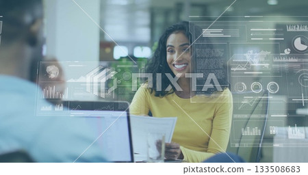 Woman in yellow top analyzing report with data overlays at modern open-plan office, with laptop 133508683