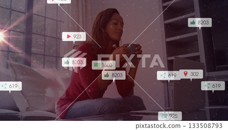 Woman holding gray mug and checking silver laptop in living room with social media icons 133508793