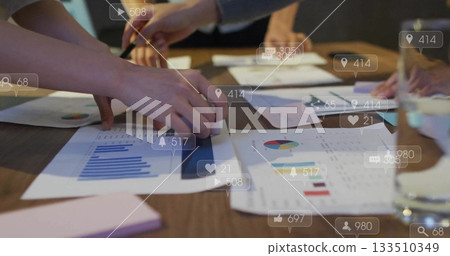 Examining professionals in suits pointing at printed graphs on meeting table with pen, sticky pad 133510349