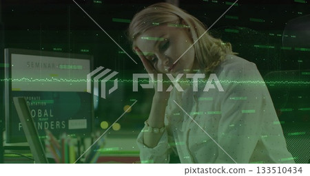 Reviewing data, woman in white blouse using laptop in office at night, with data overlay 133510434