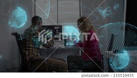 Coworkers reviewing data on desktop and laptop screens in modern office with holograms 133510435