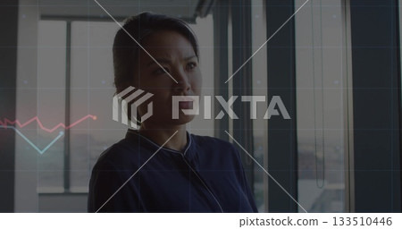 Standing Asian professional woman wearing zip-collar top near office windows, with data overlay 133510446