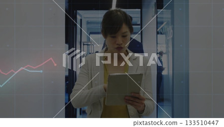 Holding tablet, Asian professional analyzing charts in office hallway with chart overlay and lights 133510447