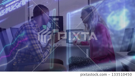 Discussing data models, man and woman gesturing and writing in notebook at office, with monitors 133510450