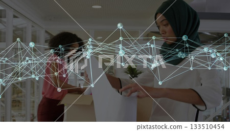 Woman in hijab and tunic unpacking board near box in office, with network overlay, copy space 133510454