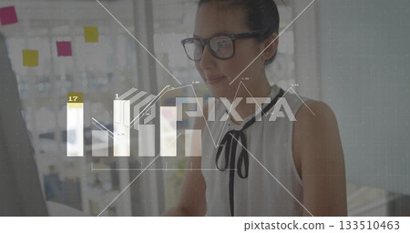 Reviewing charts businesswoman wearing glasses at office computer with glass partition notes 133510463