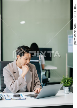 Confident Asian man with a smile standing holding notepad and tablet at office. 133511062