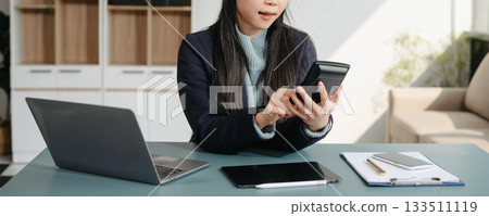 Asian businesswoman working with working notepad, tablet and laptop documents talking on the smartphone, tablet and laptop video call tax, report, accounting Asian businesswoman working with working notepad, tablet and laptop documents talking on the smartphone, tablet and laptop video call tax, report, accounting 133511119