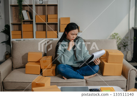 woman using smartphone or tablet taking receive and checking online purchase shopping order to preparing pack product box. 133511140