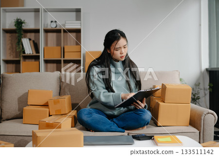 woman using smartphone or tablet taking receive and checking online purchase shopping order to preparing pack product box. 133511142
