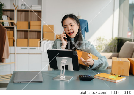 Young Asian women selling clothes on video streaming.Startup small business SME, using smartphone or tablet taking receive and checking Young Asian women selling clothes on video streaming.Startup small business SME, using smartphone or tablet taking receive and checking 133511318