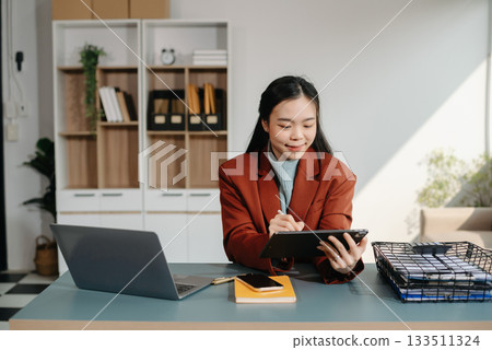 Asian businesswoman working with working notepad, tablet and laptop documents talking on the smartphone, tablet and laptop video call tax, report, accounting Asian businesswoman working with working notepad, tablet and laptop documents talking on the smartphone, tablet and laptop video call tax, report, accounting 133511324