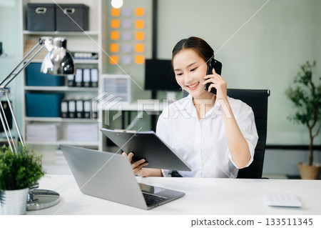 Asian businesswoman working with working notepad, tablet and laptop documents talking on the smartphone, tablet and laptop video call tax 133511345
