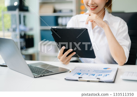 Asian woman with a smile standing holding notepad and tablet at the office. 133511350