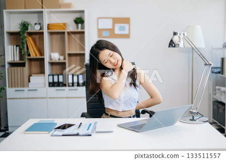 Overworked young Asian businesswoman office worker suffering from neck pain after had a long day at her office desk. Overworked young Asian businesswoman office worker suffering from neck pain after had a long day at her office desk. 133511557