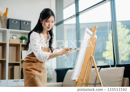 Asian Female painter do artwork in art workshop, painting supplies, oil pastels, two canvas easel, creative space 133511592