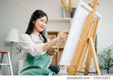 Asian Female painter do artwork in art workshop, painting supplies, oil pastels, two canvas easel, creative space Asian Female painter do artwork in art workshop, painting supplies, oil pastels, two canvas easel, creative space 133511651