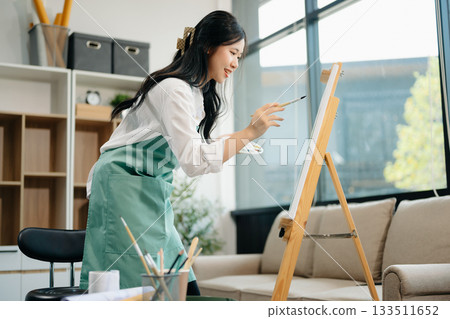 Asian Female painter do artwork in art workshop, painting supplies, oil pastels, two canvas easel, creative space 133511652