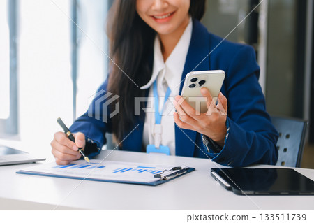 Young Asian businesswoman working with working notepad, tablet and laptop documents talking on the smartphone, tablet and laptop video call 133511739