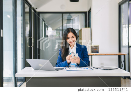 Young Asian businesswoman working with working notepad, tablet and laptop documents talking on the smartphone, tablet and laptop video call 133511741