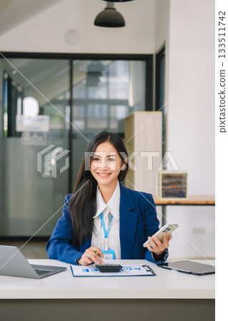 Young Asian businesswoman working with working notepad, tablet and laptop documents talking on the smartphone, tablet and laptop video call 133511742