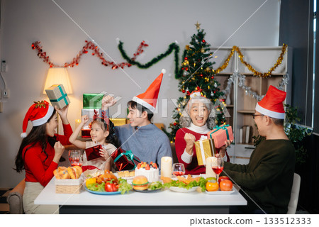 Joyful Asian family gathered for a Christmas feast, exchanging gifts, and celebrating the holiday season with love Joyful Asian family gathered for a Christmas feast, exchanging gifts, and celebrating the holiday season with love 133512333