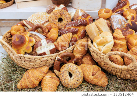 Baskets overflowing with different kinds of bread variety of shapes in local bakery setting. 133512404