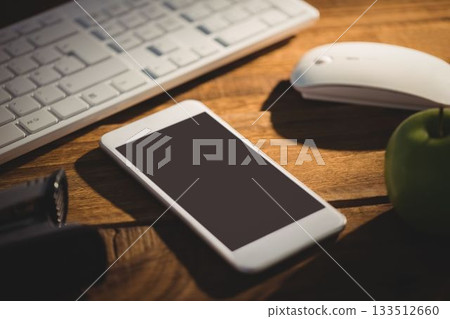 Smartphone is sitting on wood desk in flat design, with keyboard and mouse, flashlight, green apple 133512660