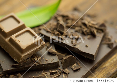 3D render showing milk and dark chocolate pieces resting on rustic wooden board with green leaf 3D render showing milk and dark chocolate pieces resting on rustic wooden board with green leaf 133513029