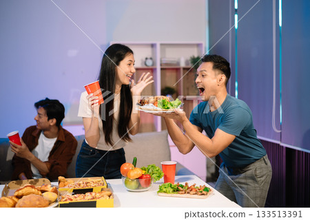 Young Asian Friends Celebrating with Laughter and Food at a Modern Evening Party 133513391