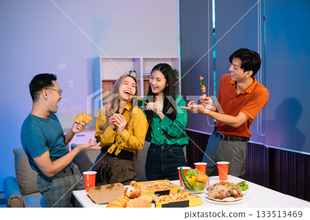 Young Asian Friends Celebrating with Laughter and Food at a Modern Evening Party 133513469